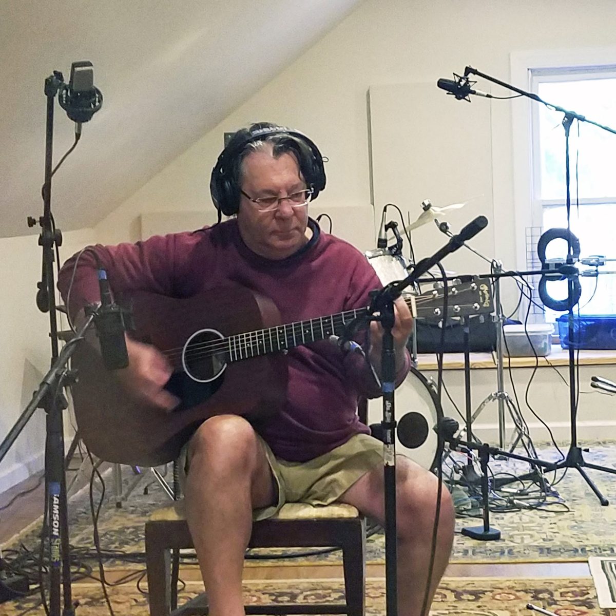 Dayna Wittman playing acoustic guitar in a studio, surrounded by microphones.